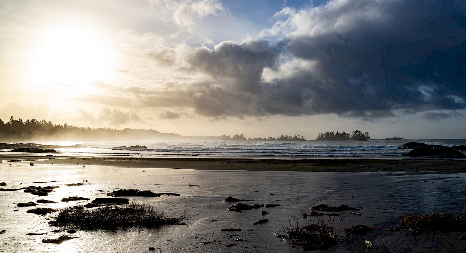 Sun shining through the clouds and reflecting on Chesterman Beach while storm clouds gather