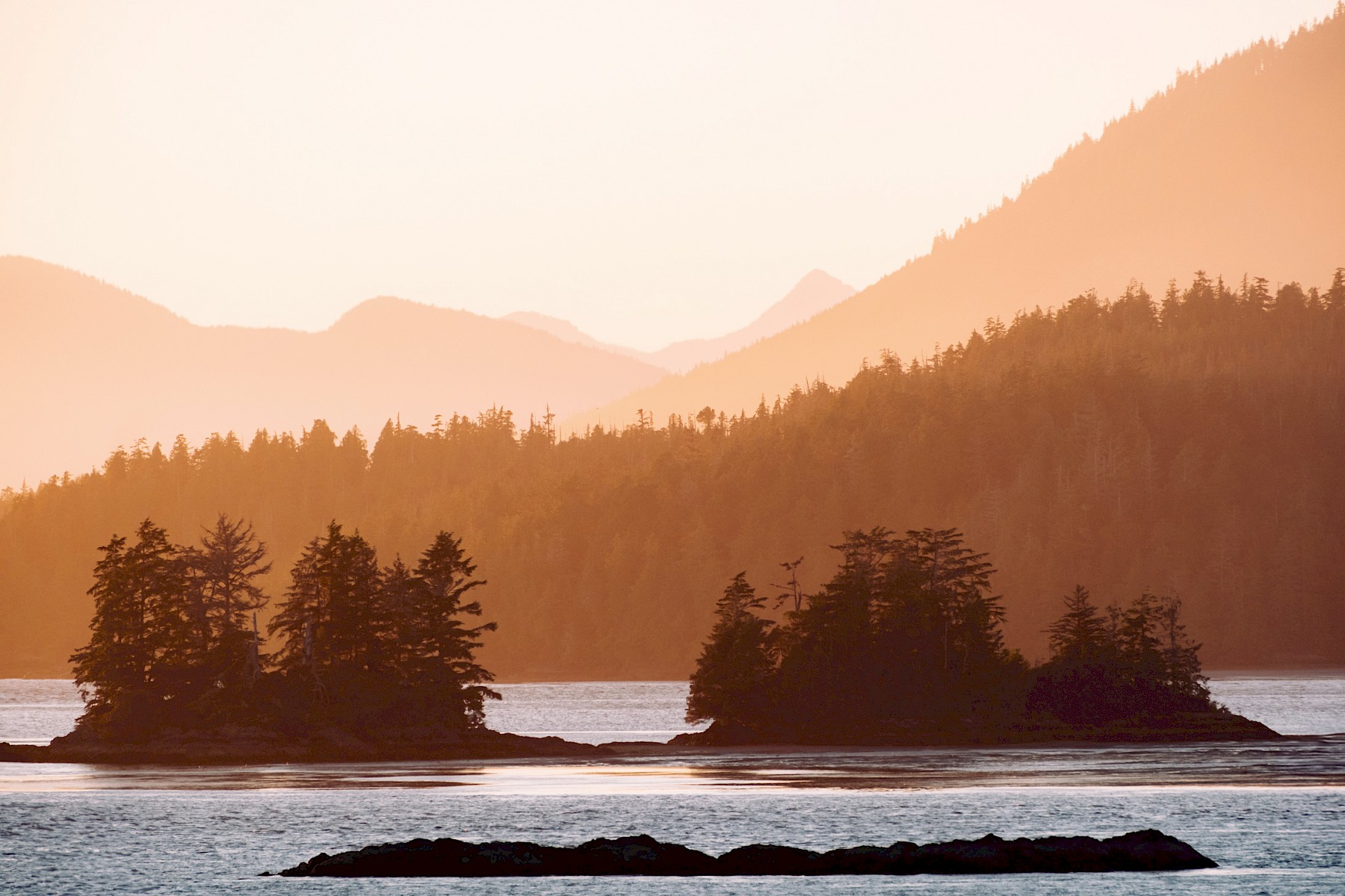 Tofino Inlet at sunset with small forested islets and layered mountain silhouettes