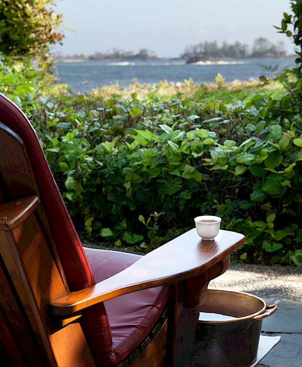 Wooden spa chair with a cup of tea on the armrest overlooking ocean and salal foliage