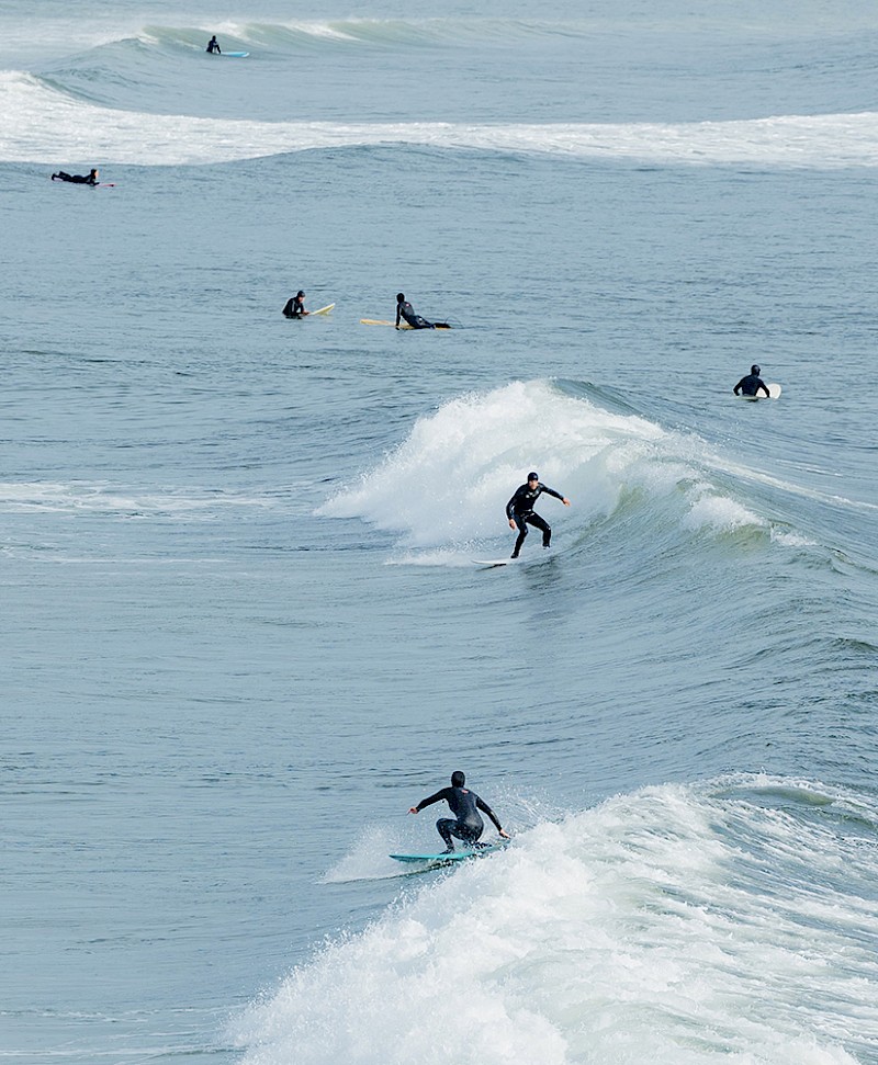 Surfers riding waves in the ocean, with several others waiting their turn.