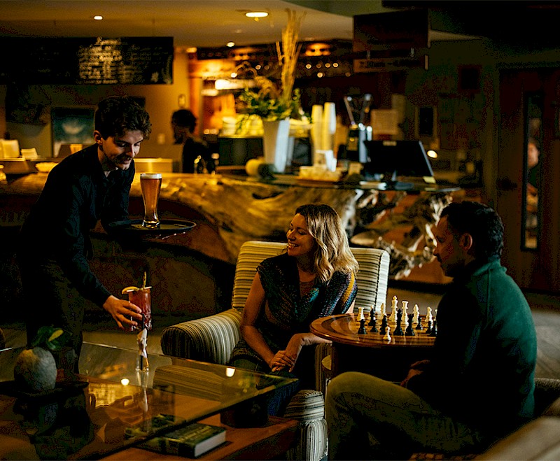 A server delivering drinks to a couple playing chess in a cozy, wood-accented café lounge