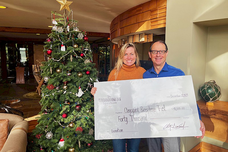 Charles McDiarmid and Michelle Hall holding a large ceremonial check for Clayoquot Biosphere Trust for $40,000 in a room decorated with a Christmas tree.