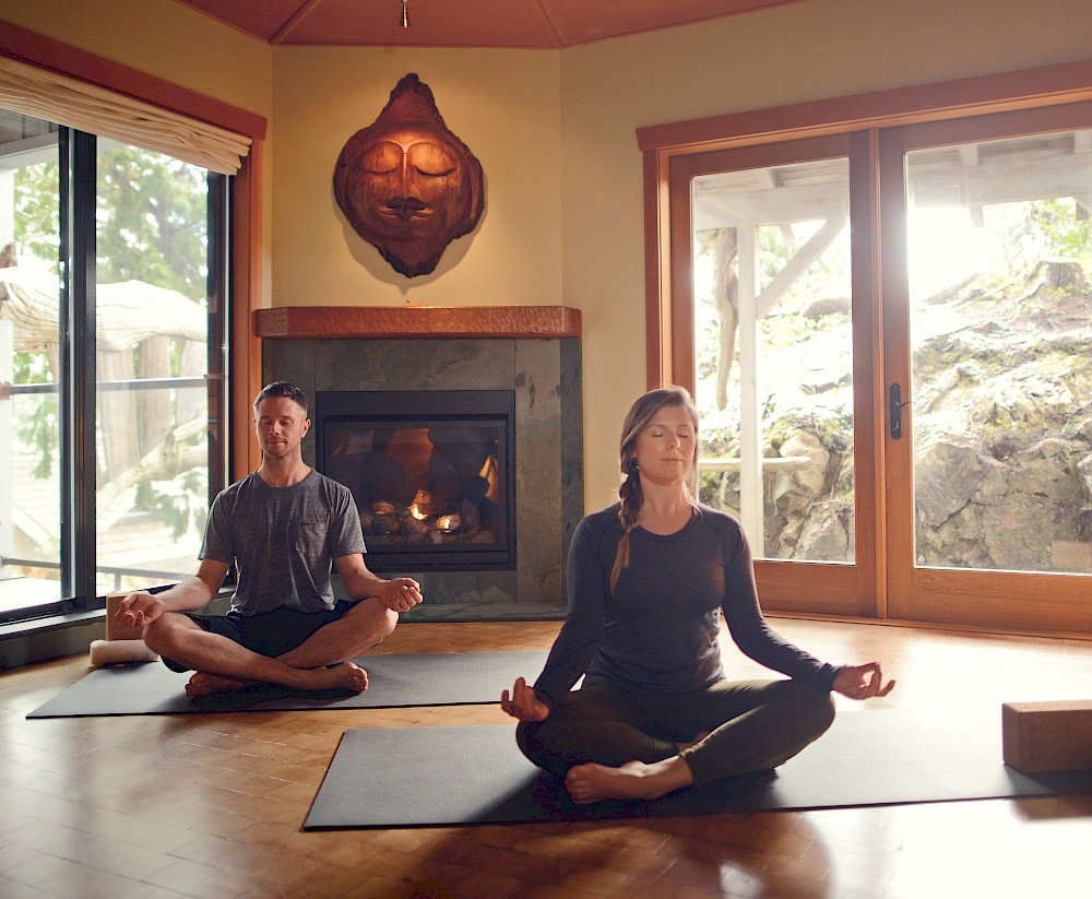 Two guests practicing yoga inside the spa's Haven room beside a glowing fireplace
