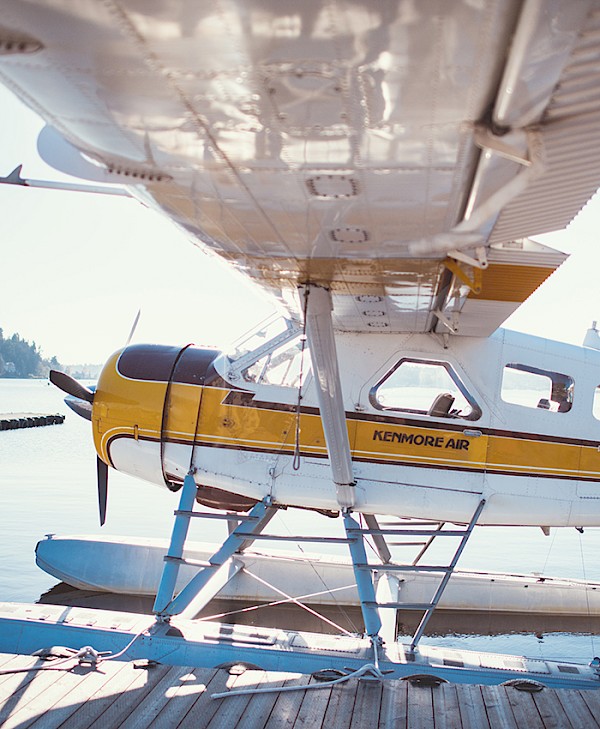 A Kenmore Air float plane parked at a wooden dock, with clear skies and calm water visible in the background