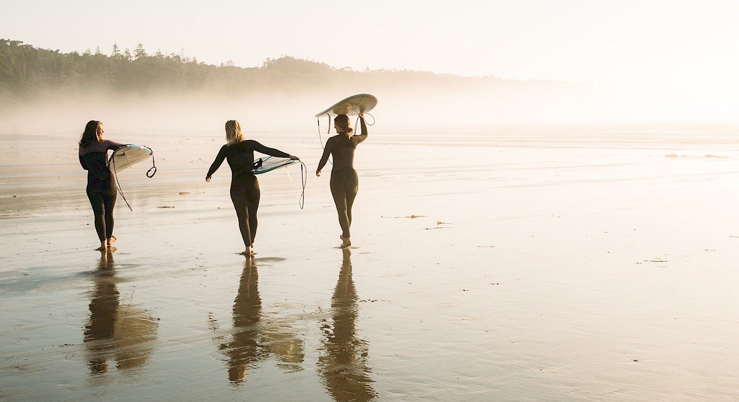 Three surfers walk along Chesterman Beach with their surfboards