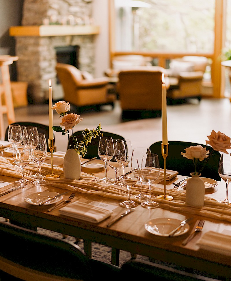 A wedding table setting in the foreground with cozy chairs grouped around a stone fire in the background