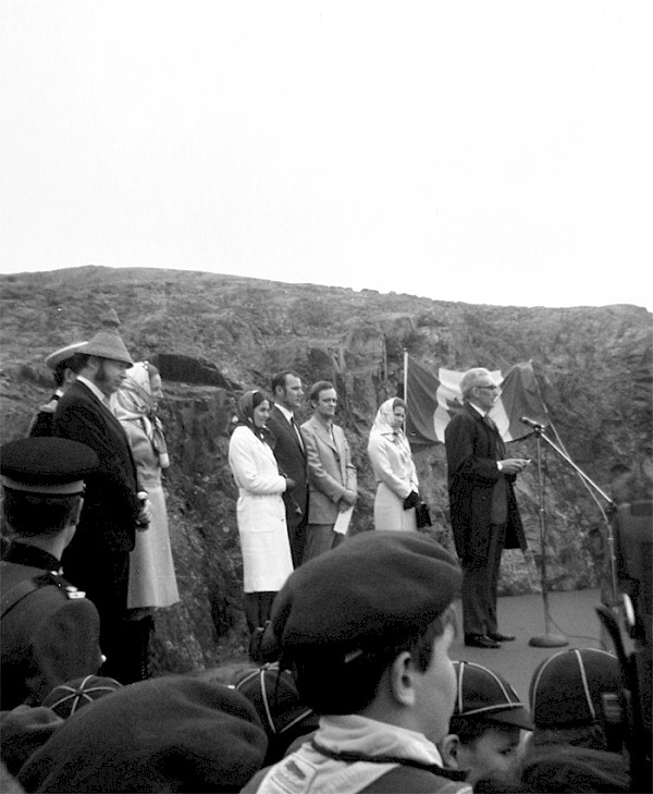 Dr. Howard McDiarmid speaking on stage during an outdoor ceremony with dignitaries behind him