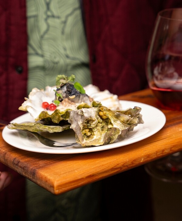 Plate of various flavoured oysters on a wooden tray with a glass of red wine in the background