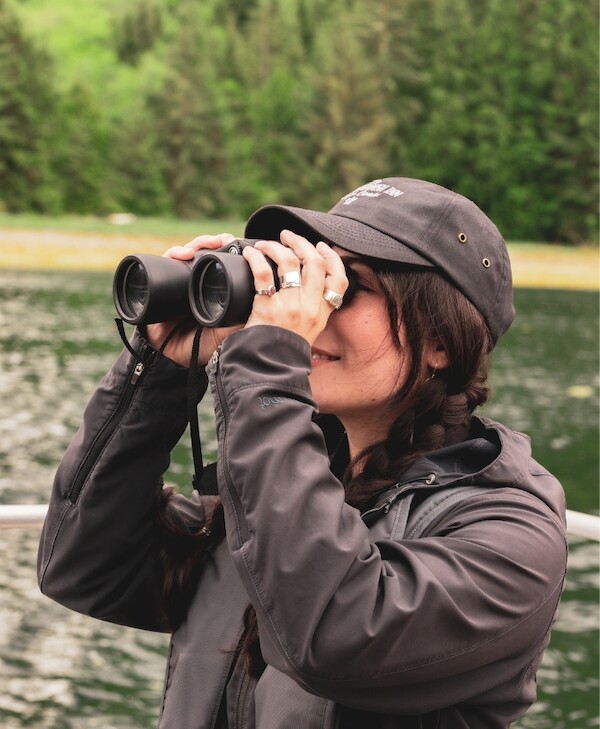 A woman on a boat uses binoculars to spot wildlife in the distance