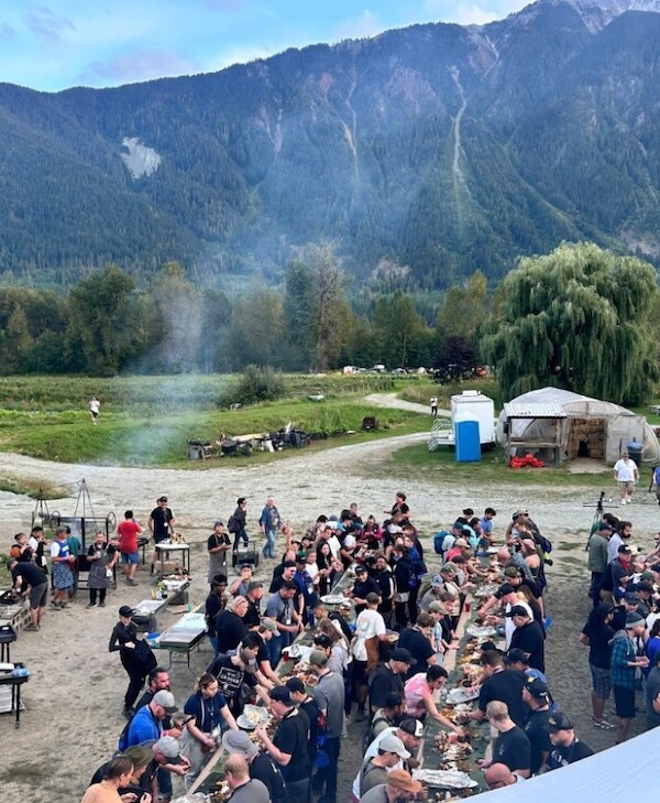 A beautiful BC mountainside serves as the backdrop for tables of CooksCamp attendees lined up to enjoy various culinary creations