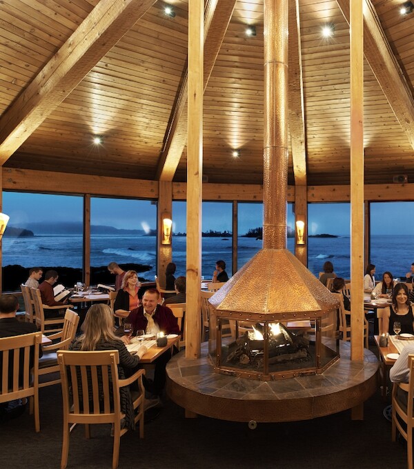 Guests dining at The Pointe Restaurant around the central copper fireplace. They are seated in the restaurant's original high-backed dining chairs.