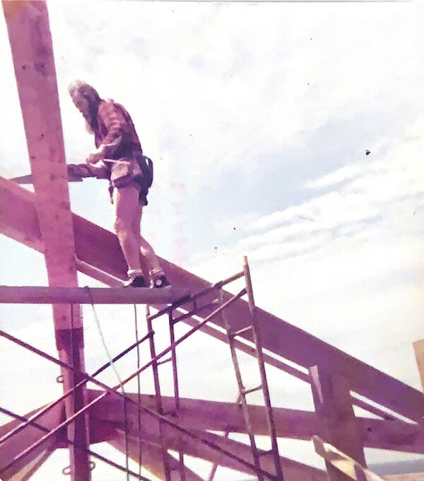 A man (Henry Nolla) saws at a wooden beam in an old photo taken during the construction of the family cabin