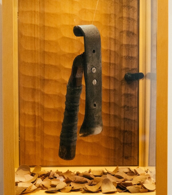 Henry's handmade hand-adze in a display case with the cedar shavings it creates down below